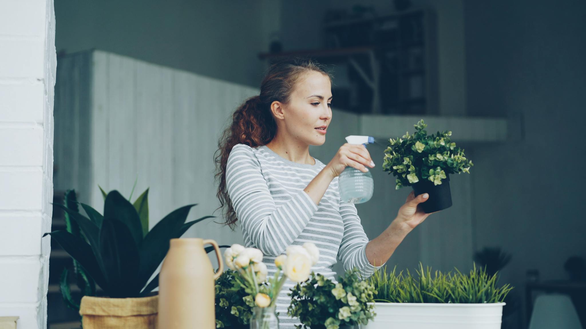 A woman waters potted plants indoors, enjoying a gardening moment at home.